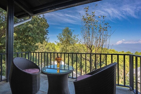 A balcony with wicker furniture and a glass table, overlooking a forested area. - Seed at Queens Meadows Ranikhet (Ranikhet)