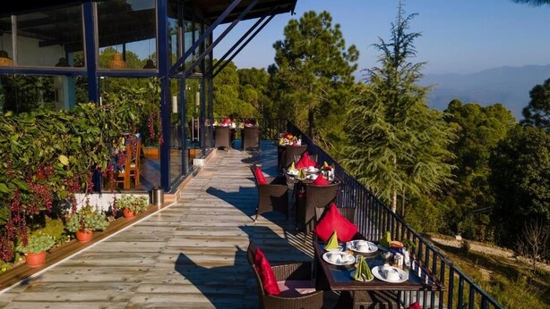 Une terrasse en bois avec des sièges extérieurs et un espace abrité, entourée d’une végétation luxuriante et d’arbres.