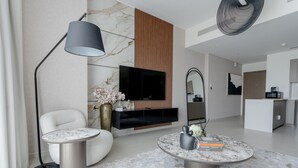 Un salon moderne avec une cheminée en marbre, un téléviseur à écran plat, une table basse ronde et un fauteuil blanc.