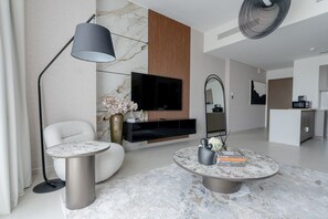 A modern living room with a marble fireplace, a flat-screen TV, a round coffee table, and a white armchair. - Luxurious - Grande Signature - Downtown (Dubai)