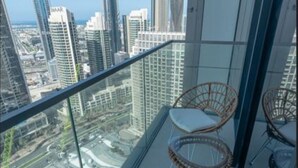 Un balcon doté de chaises en osier et d’une rambarde en verre, offrant une vue sur un paysage urbain avec de hauts immeubles.