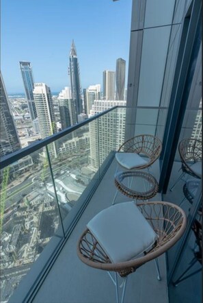 A balcony with wicker chairs and a glass railing overlooking a cityscape with tall buildings. - Luxurious - Grande Signature - Downtown (Dubai)