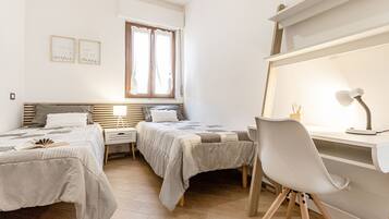 Een slaapkamer met twee bedden, een bureau met stoel, een raam met gordijnen en een nachtkastje met lamp.