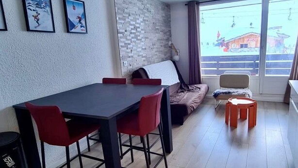 Ein modernes Wohnzimmer mit Esstisch, roten Stühlen, einer Couch und einem großen Fenster mit Blick auf ein Gebäude.