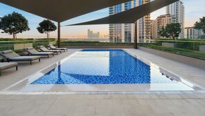 A rooftop pool with lounge chairs, a shaded canopy, and a cityscape view. - Serene 1BR Escape with Burj Khalifa View (Dubai)