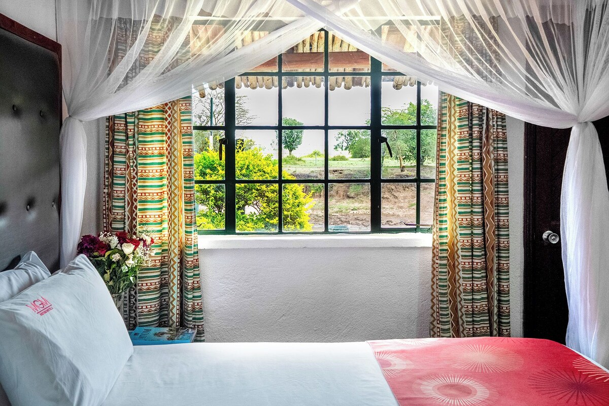 Une chambre à coucher avec un lit, une fenêtre avec des rideaux et une vue sur la verdure à l’extérieur.