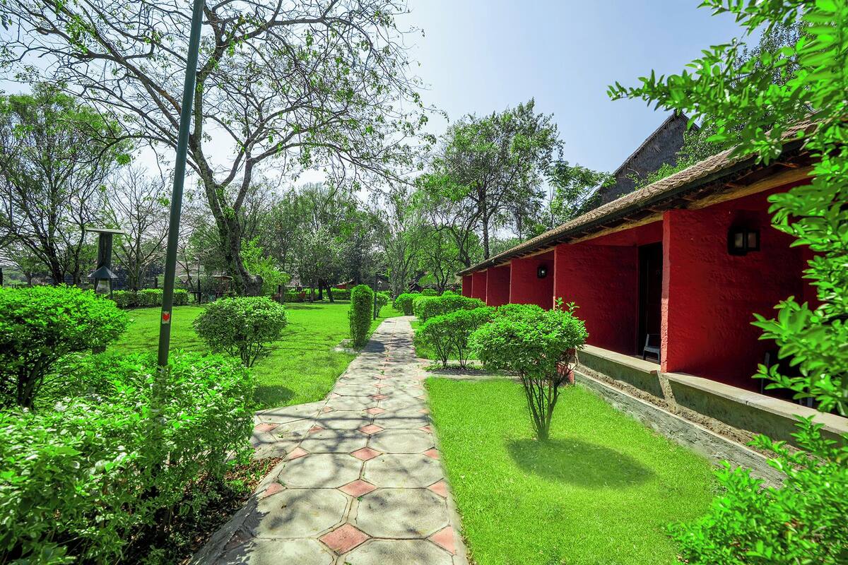 A red building with a thatched roof, surrounded by well-maintained green lawns and trees.