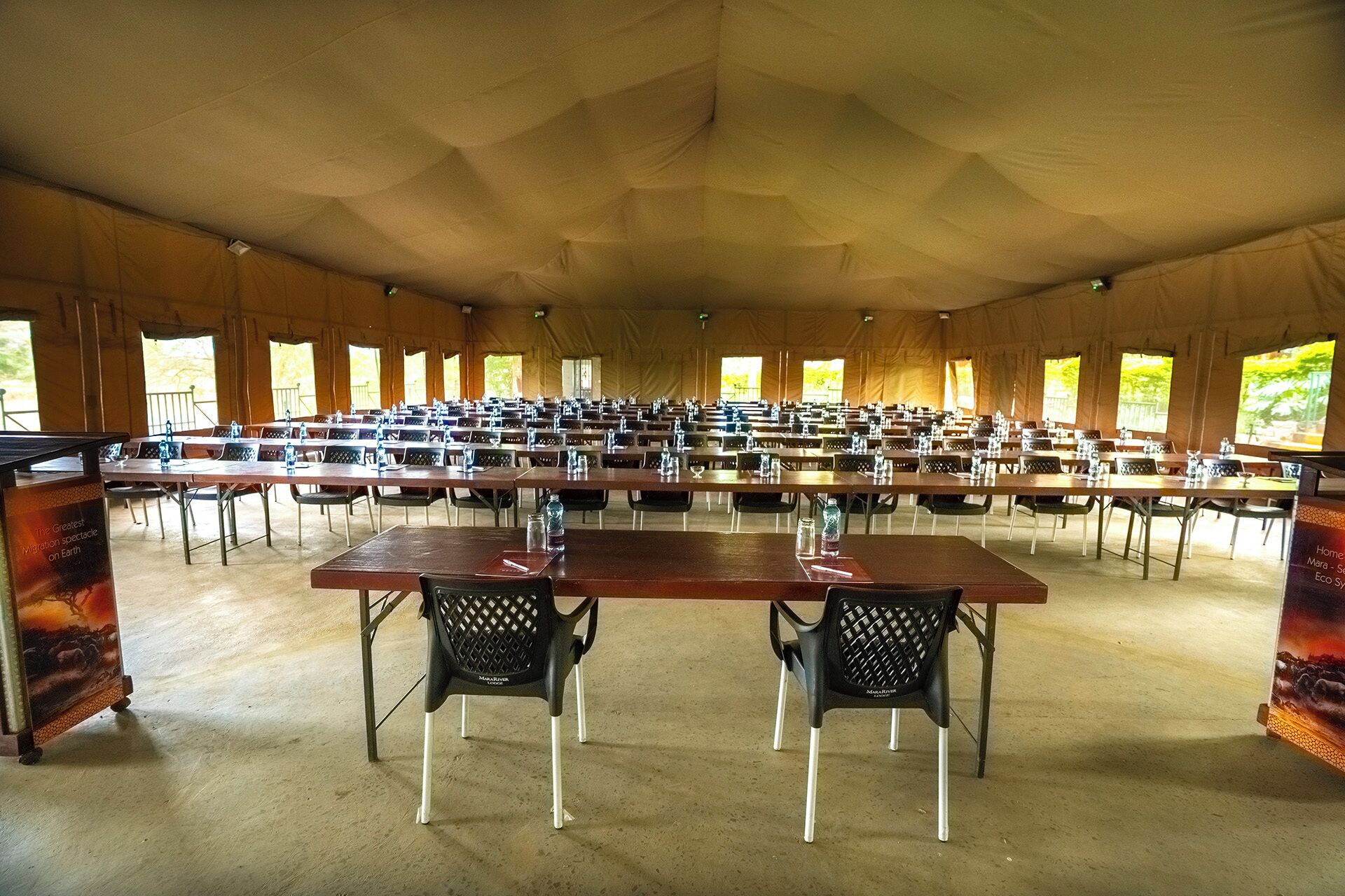 A large tented dining area with numerous tables and chairs, arranged in rows.