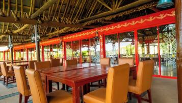 A restaurant with a thatched roof, wooden tables, and chairs.
