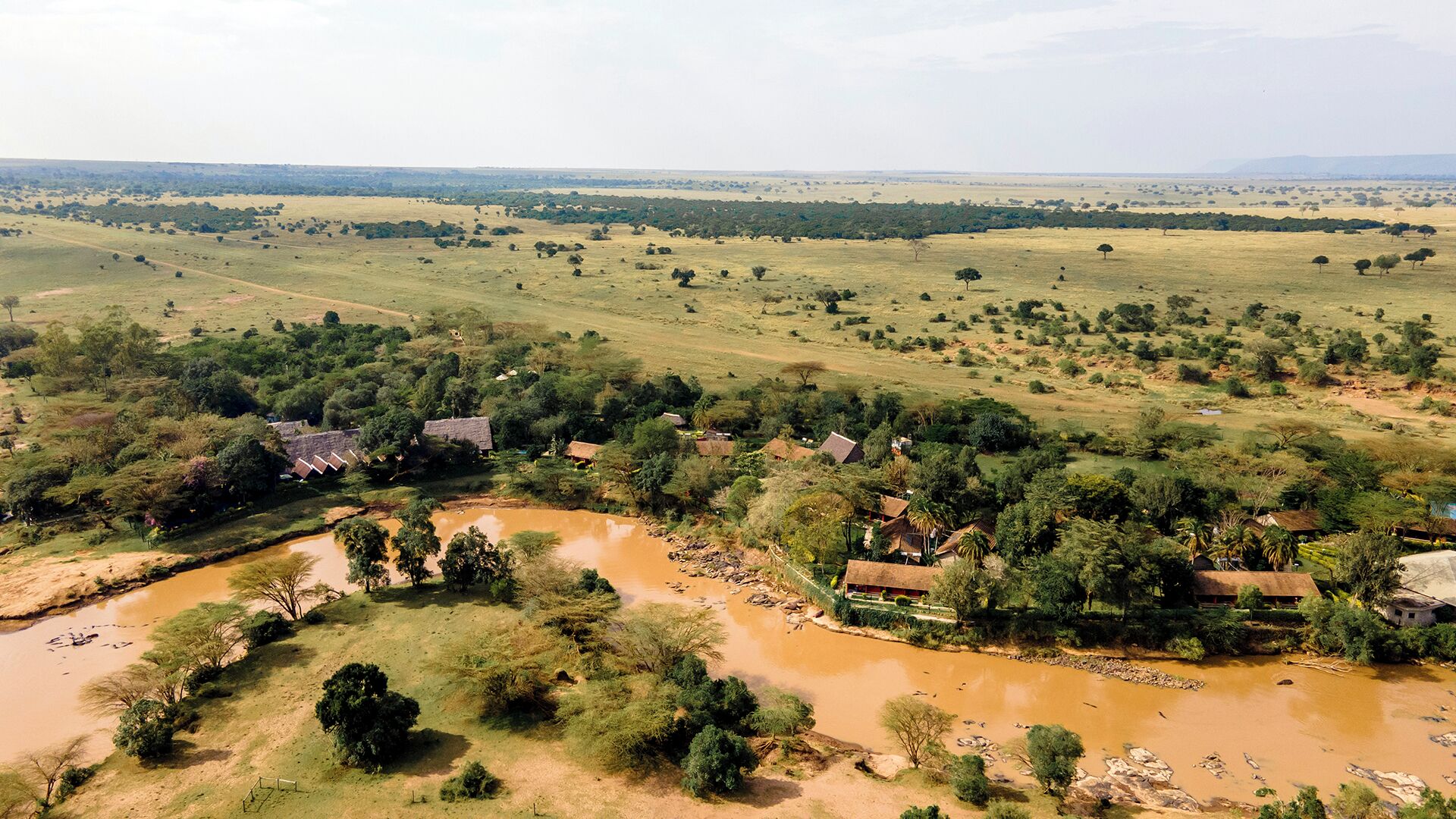 Paisagem rural com casas isoladas, um rio e um extenso campo aberto.