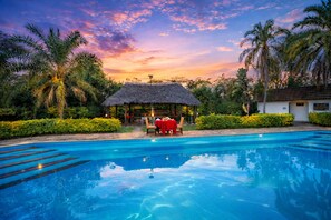 A swimming pool with a thatched-roof pavilion and palm trees. - Muthu Mara River Lodge  (Maasai Mara)