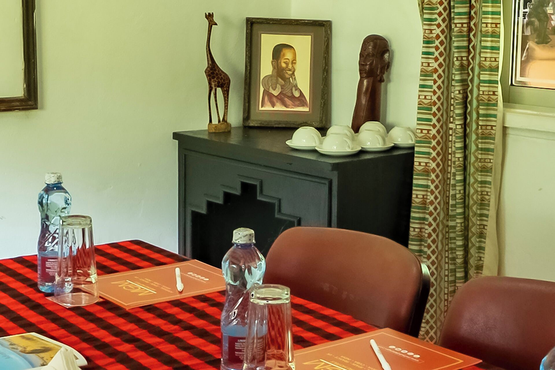 Un salón de conferencias con mantel a cuadros, un armario de madera con un retrato enmarcado y una figurita de jirafa.