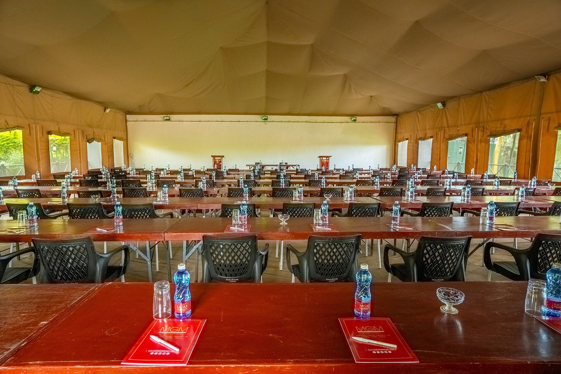 Une grande salle de conférence, avec de nombreuses rangées de tables et de chaises, chaque table étant équipée de bouteilles d’eau et de verres.
