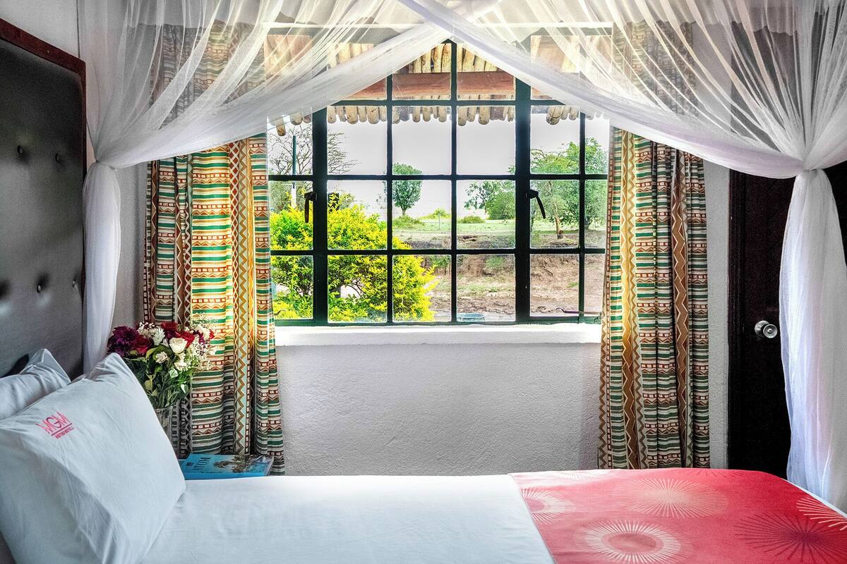 A bedroom with a bed, a window with curtains, and a view of greenery outside.