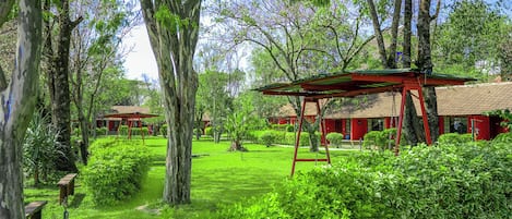 Un exuberante jardín con un columpio, rodeado de árboles y un edificio de techo rojo.