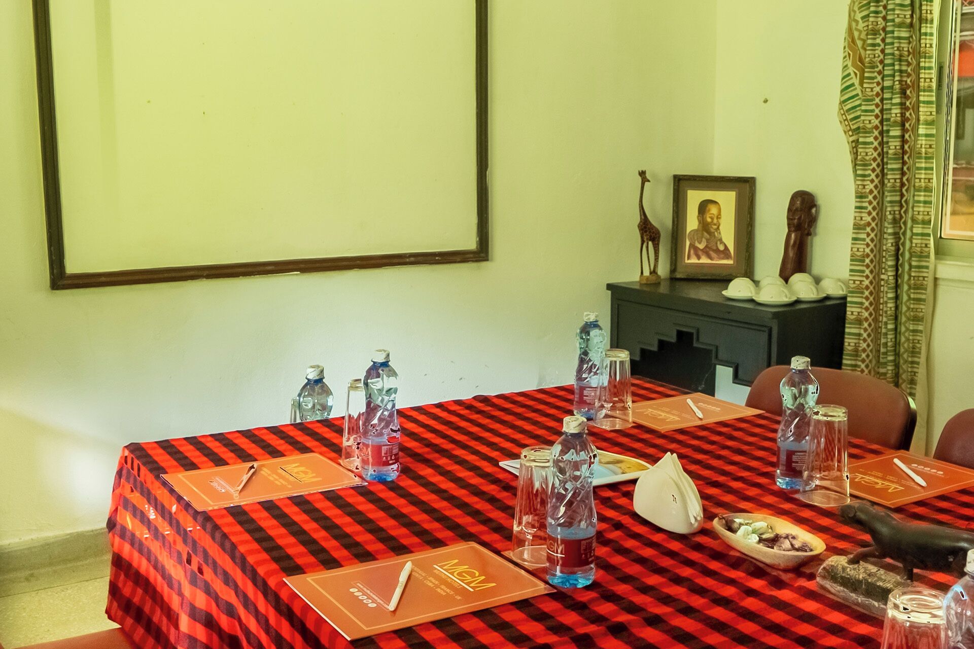 A conference room with a red and black checkered tablecloth, water bottles, a plate of food, and a framed picture on a shelf.