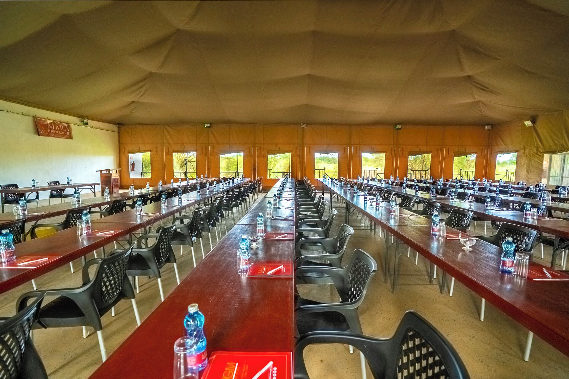 A large tented conference room with long tables and chairs, equipped with water bottles and glasses.