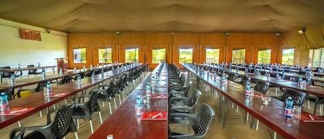 A large tented conference room with long tables and chairs, equipped with water bottles and glasses.