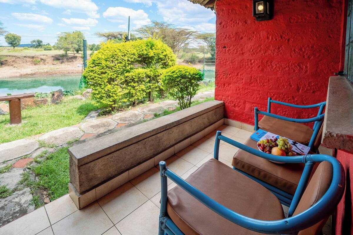 A balcony with a red wall, a blue chair, and a table with a fruit basket.