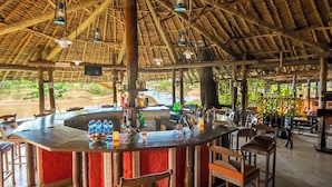 A bar area with a thatched roof, wooden furniture, and a view of the outdoors.