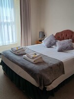 Uma cama bem arrumada com travesseiros, um abajur e uma janela com cortinas.