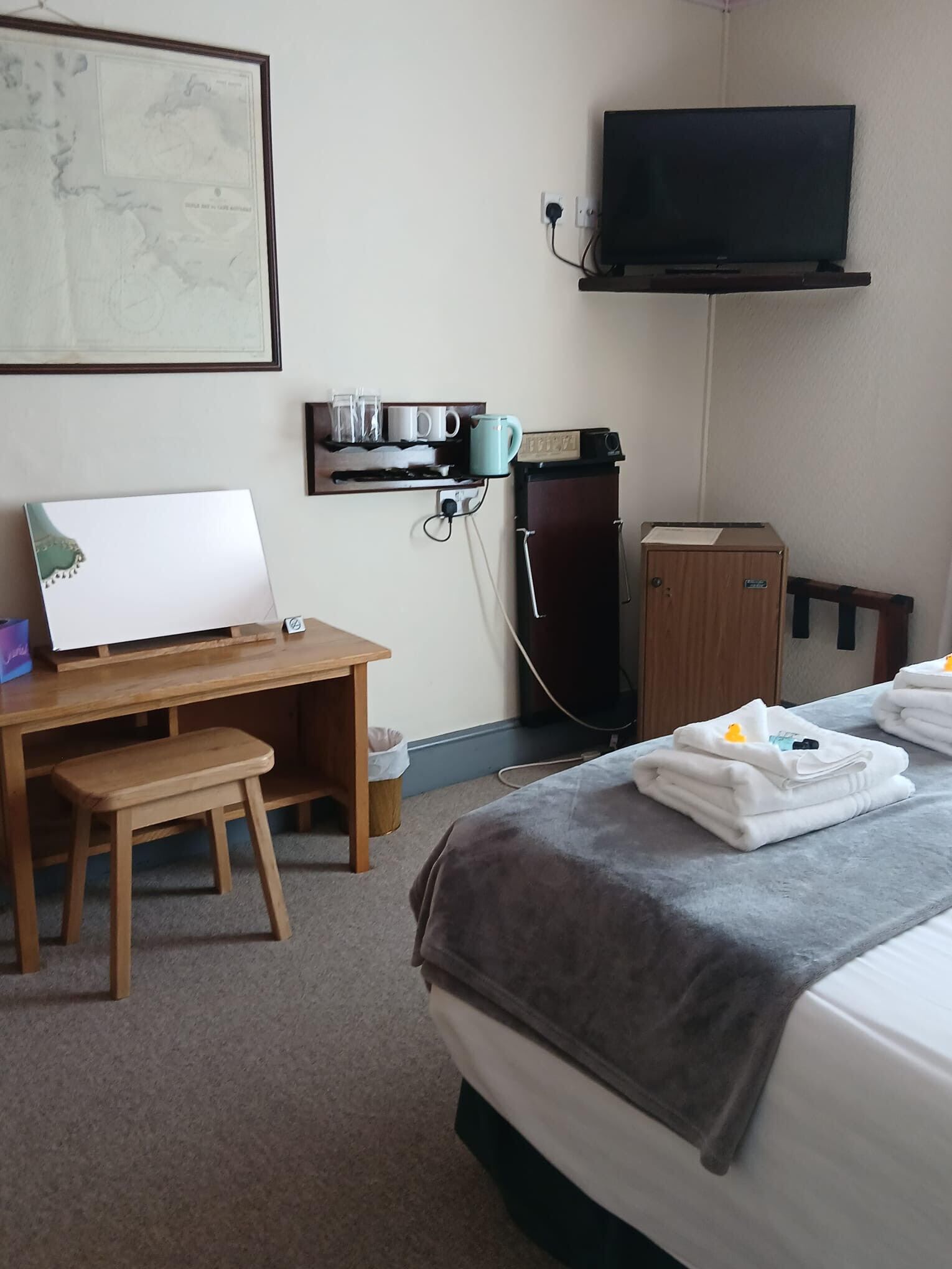 Een hotelkamer met een bed, een bureau, een stoel, een aan de muur bevestigde televisie en een klein kastje.