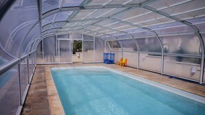 Uma piscina com cobertura de vidro, uma cadeira azul e uma cadeira laranja.