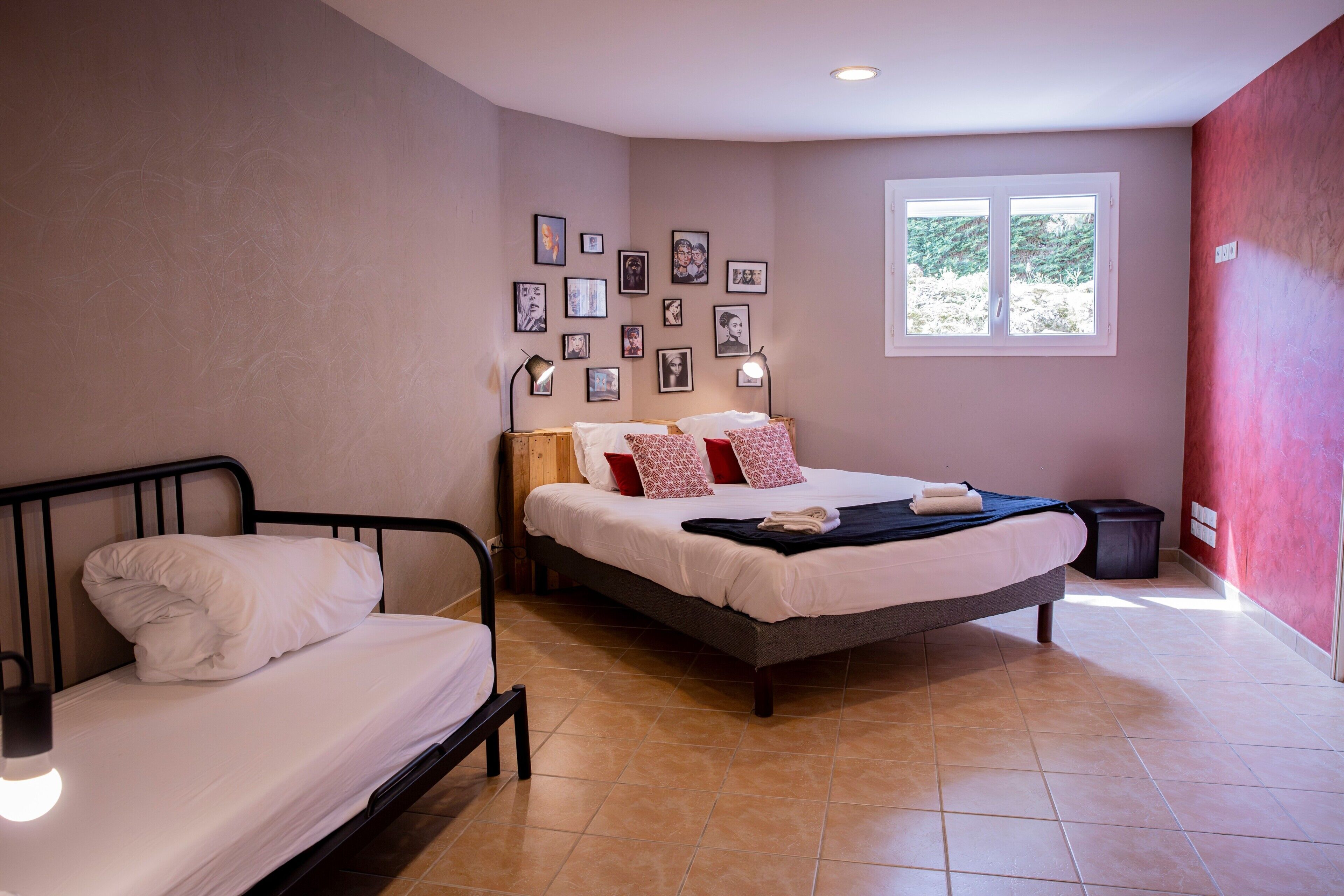 Une chambre à coucher avec un lit, un petit lit, une fenêtre et des tableaux accrochés au mur.