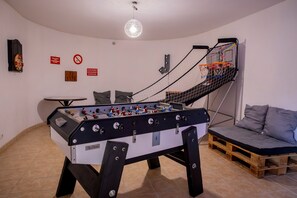 A room with a foosball table, a sofa, and a basketball hoop. - Holiday Home 'L'Escale Des Copains' with Private Pool, Private Terrace and Wi-Fi (Cormeray)