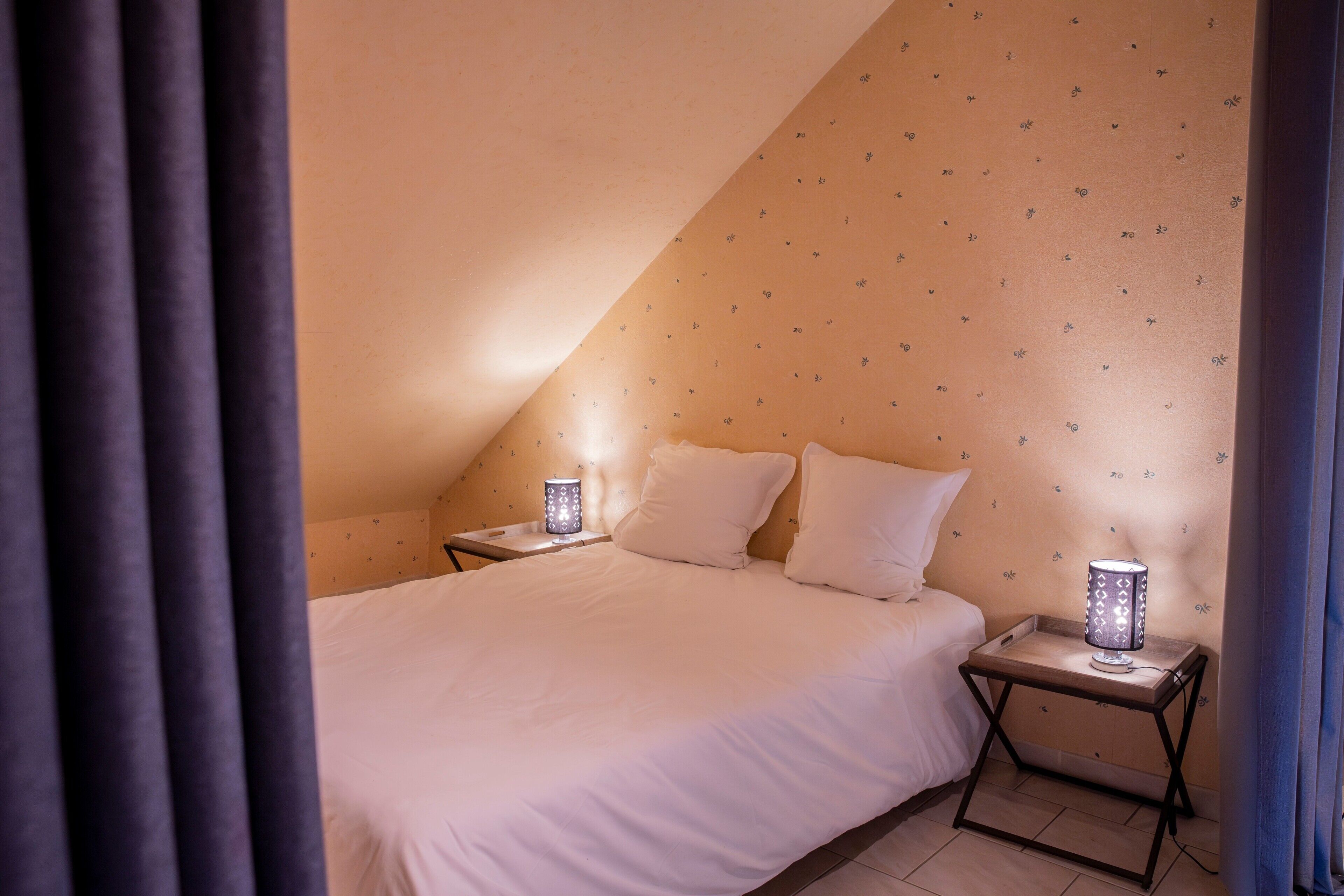 Quarto com cama, duas mesas de cabeceira com abajures e parede estampada.