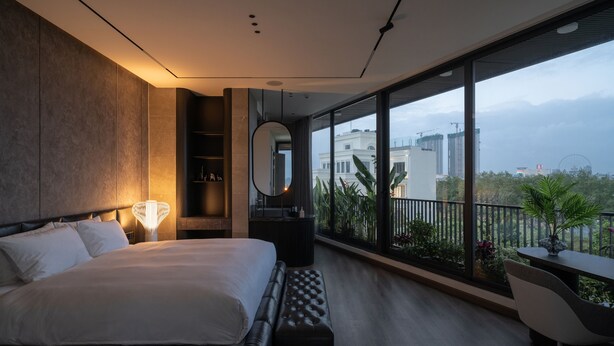 Ein modernes Schlafzimmer mit einem großen Bett, einem Nachttisch, einem Spiegel und Blick auf die Stadt durch große Fenster.