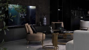 Ein modernes Wohnzimmer mit großem Flachbildfernseher, einer Couch, einem Couchtisch und einer Küchenzeile im Hintergrund.