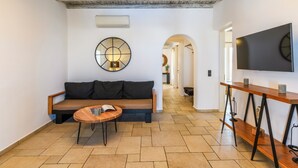 Un soggiorno moderno con una panca in legno, un tavolino rotondo e un grande televisore a parete.