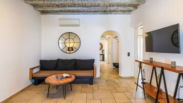 Una sala de estar moderna con un banco de madera, una mesa redonda de centro y un televisor grande montado en la pared.