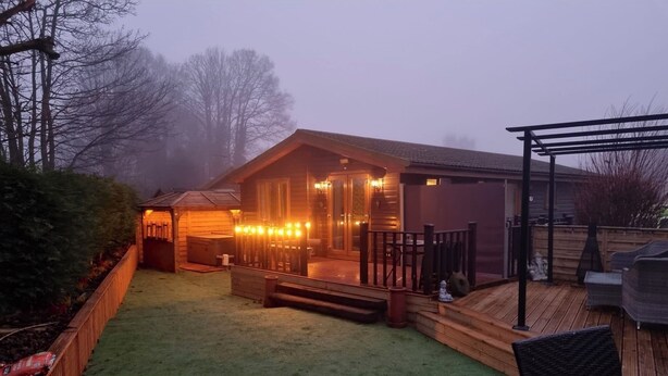 A wooden cabin with a deck, a hot tub, and a covered patio area.