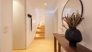 Un couloir avec un escalier en bois, un vase contenant des fleurs séchées et un miroir accroché au mur.