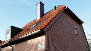 A two-story brick building with a red-tiled roof, a visible chimney, and a large garage door. - Vacation home in Tossens - relaxation for the whole family. (Butjadingen)