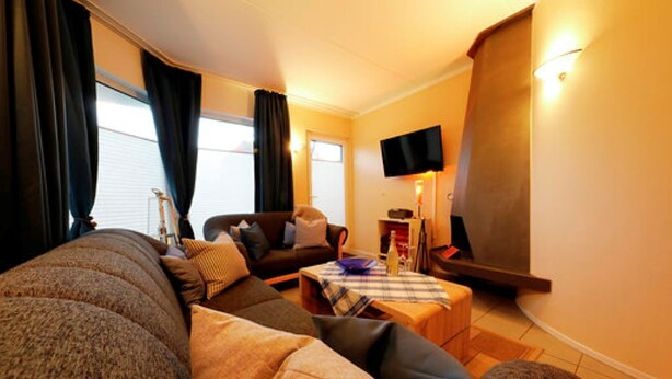 A cozy living room with a sofa, a small table, and a flat-screen TV mounted on the wall. - Vacation home in Tossens - relaxation for the whole family. (Butjadingen)