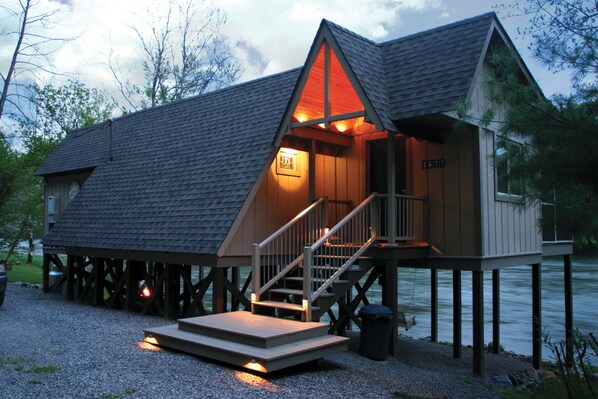 A cabin with a wooden deck, a staircase, and a view of the water.