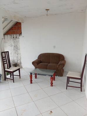Um quarto com um sofá marrom, uma mesa com tampo de vidro e duas cadeiras de madeira.