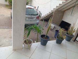 A balcony with potted plants, a white car parked outside, and a TV on a wall. - Lar Jampa Praias Sul (Conde)