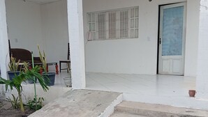A building entrance with concrete steps leading to a door, a small garden area with potted plants, and a window with shutters. - Lar Jampa Praias Sul (Conde)