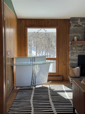 Eine moderne Küche mit Holzvertäfelung, einer Glasarbeitsplatte, einem Kamin aus Stein und einem schwarz-weiß gestreiften Teppich.