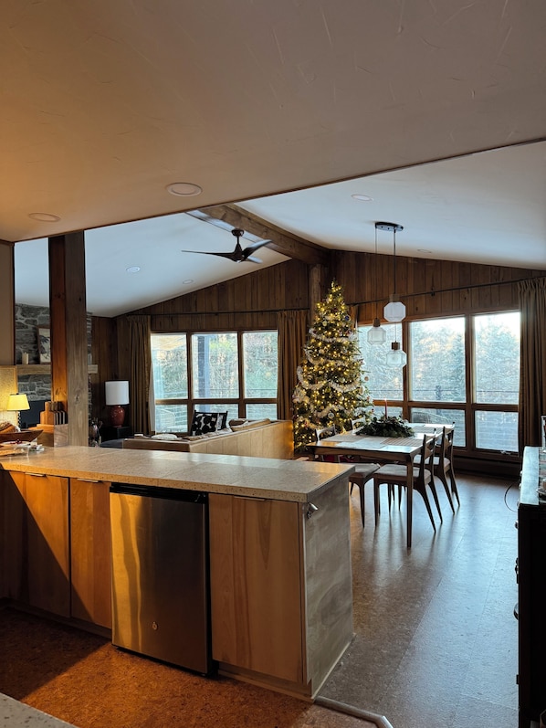 A modern kitchen with a central island, wooden beams, large windows, and a Christmas tree.