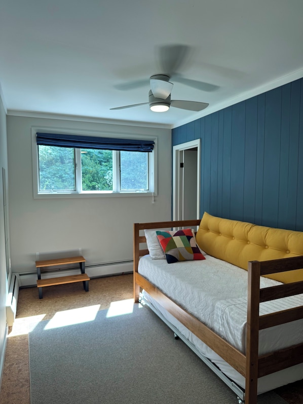 Ein Schlafzimmer mit einem Bett, einem Deckenventilator, einem Fenster mit Blick, einer Bank und einer Tür.