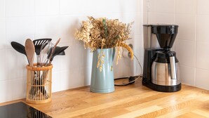 Un plan de travail de cuisine avec une machine à café, un vase contenant des fleurs séchées et un porte-ustensiles.