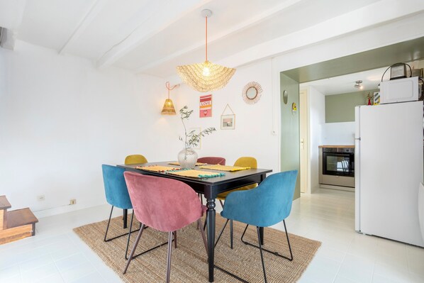 Ein Essbereich mit einem schwarzen Tisch, bunten Stühlen, einer gewebten Pendelleuchte und einer Küche im Hintergrund.