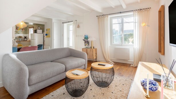 Un salon moderne avec un canapé gris, deux tables rondes à plateaux tressés, une table basse en bois et un téléviseur fixé au mur.