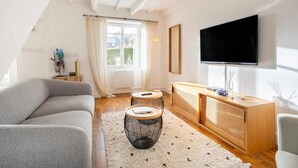 Un salon moderne avec un canapé gris, deux petites tables d’appoint rondes, une console en bois et un téléviseur à écran plat fixé au mur.