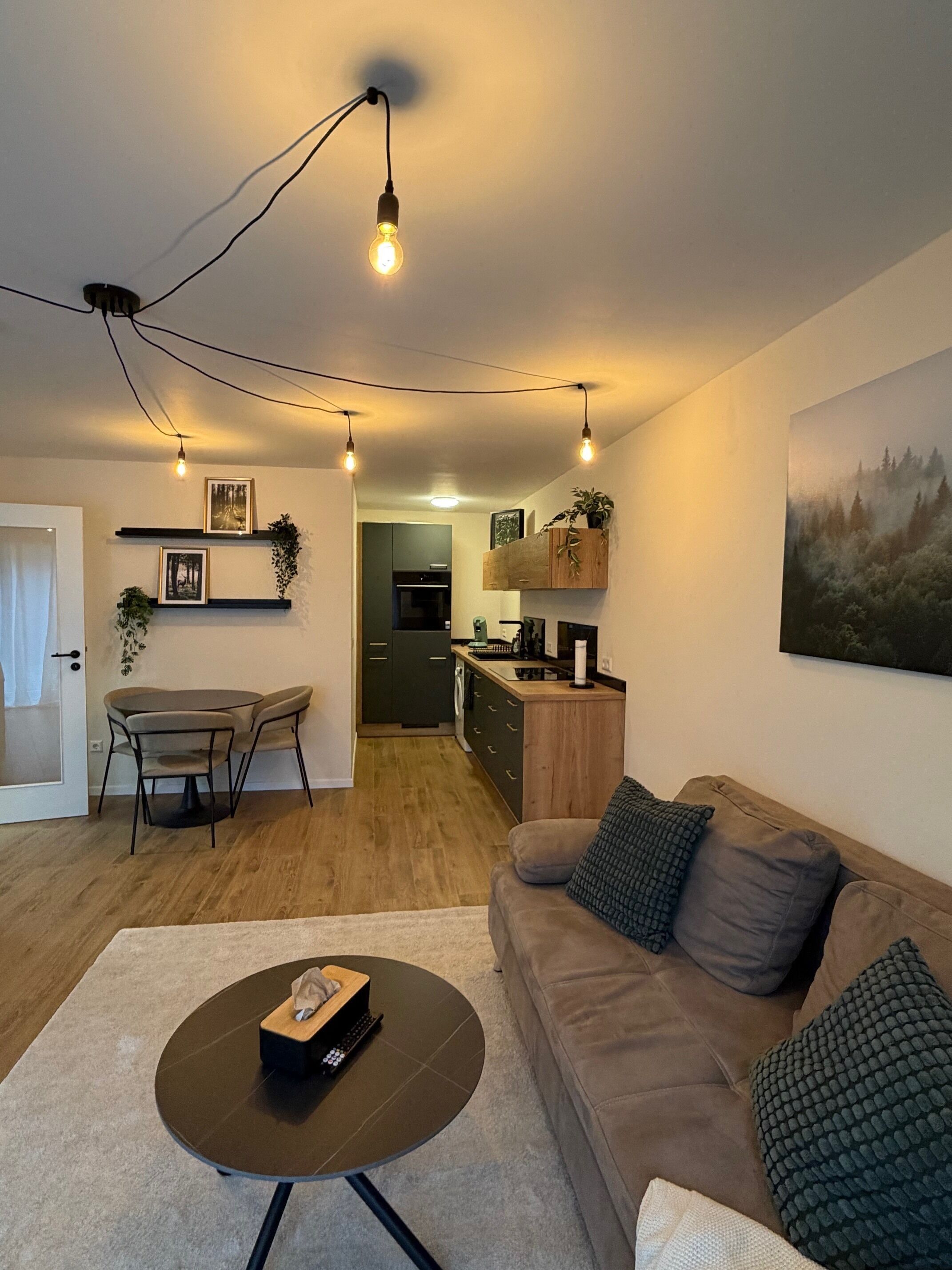 A modern living room with a sofa, coffee table, and dining area. There is a kitchen in the background with cabinets and a refrigerator.